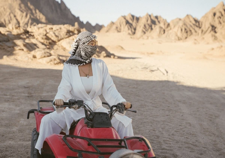 A woman riding a red ATV through the mountains, representing An Unforgettable Desert Adventure.