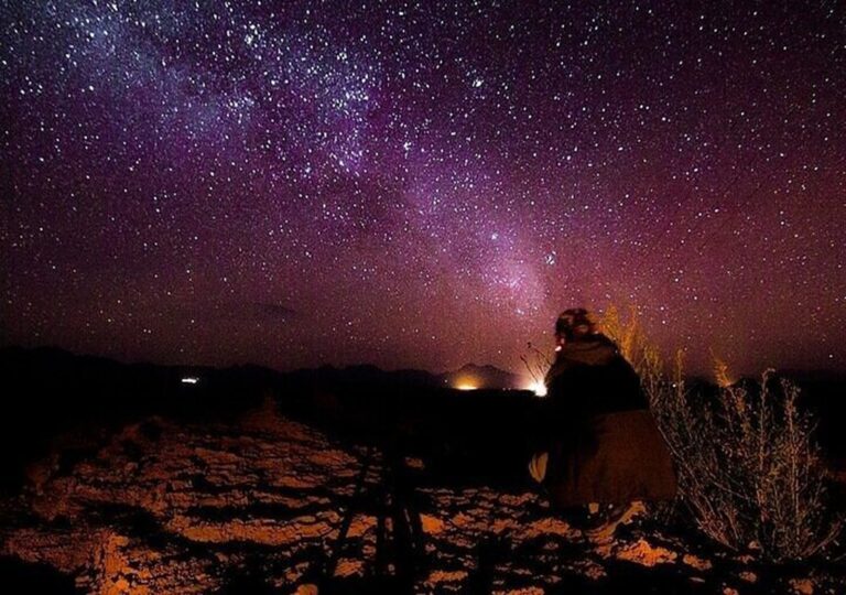 A traveler following The Ultimate Guide to Stargazing in the Hurghada desert under a vibrant Milky Way sky.