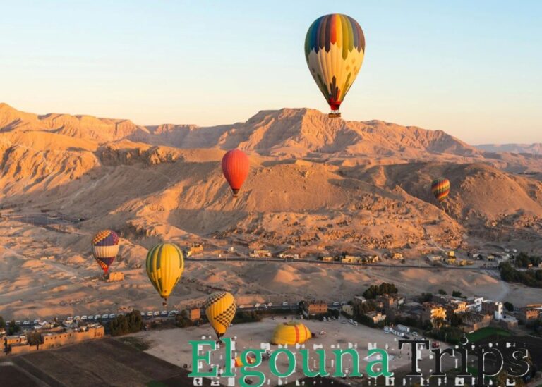 A fleet of colorful hot air balloons floating gently over the desert mountains and ancient ruins during a sunrise hot air balloon Luxor tour in Egypt.